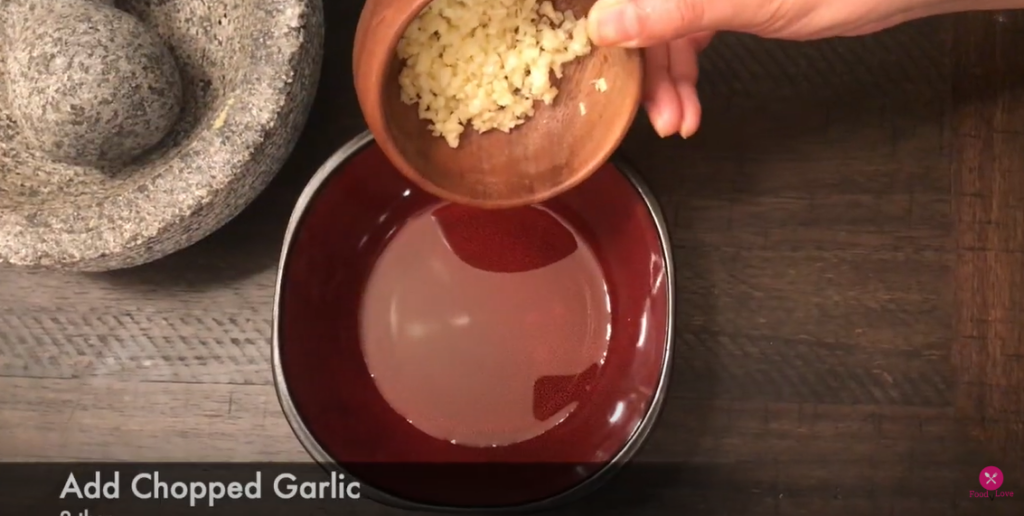 a hand transferring chopped garlic from one bowl to another